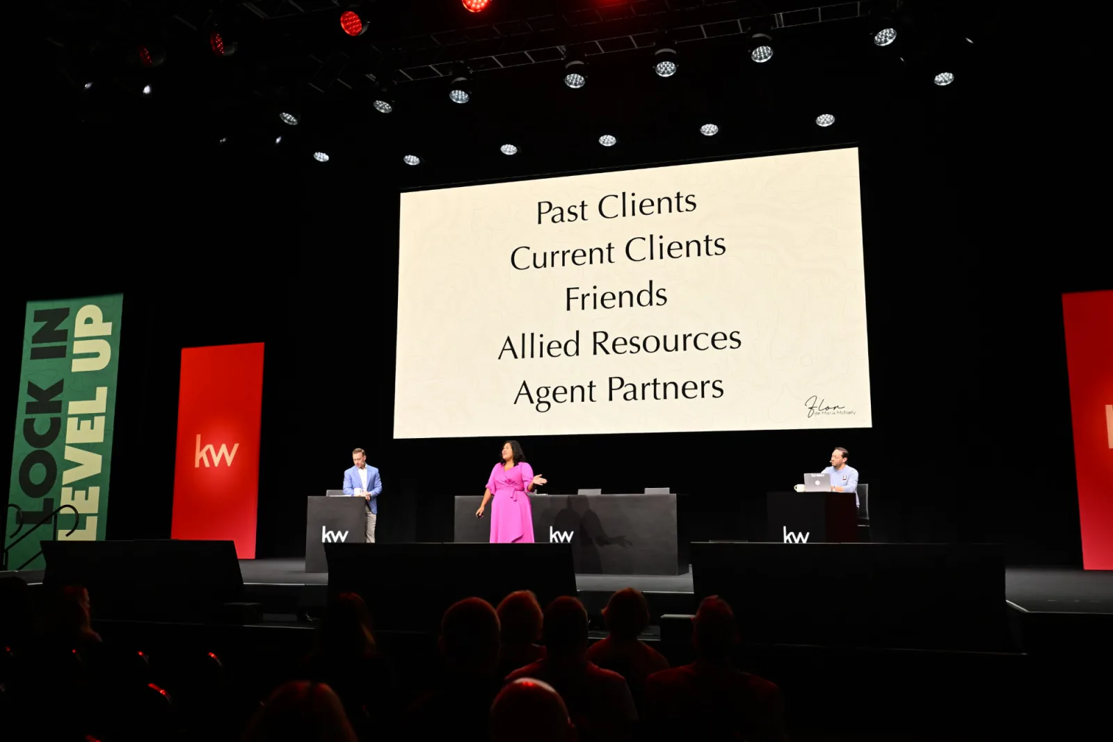 Flor on a large stage presenting a slide that lists past clients, current clients, friends, allied resources and agent partners